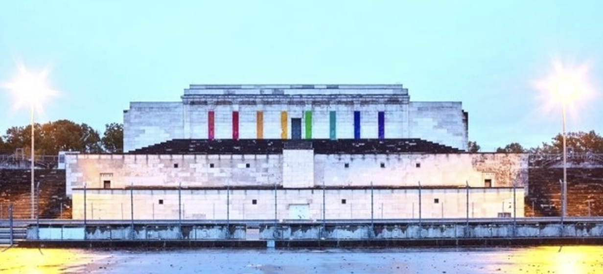 Großes steinernes Gebäude mit bunten senkrechten Streifen, zwei Laternen und nassem Vorplatz bei Dämmerung